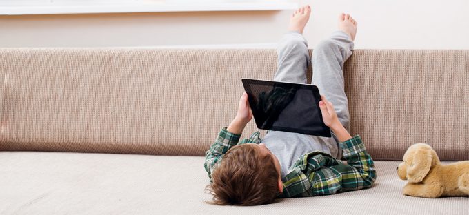 Kid laying on a couch looking at ipad