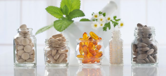 Glass bottles filled with various supplement capsules on a white counter top