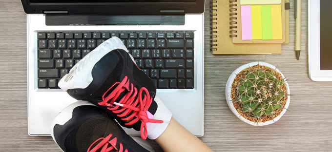 Business woman resting feet with workout shoes on desk with open laptop