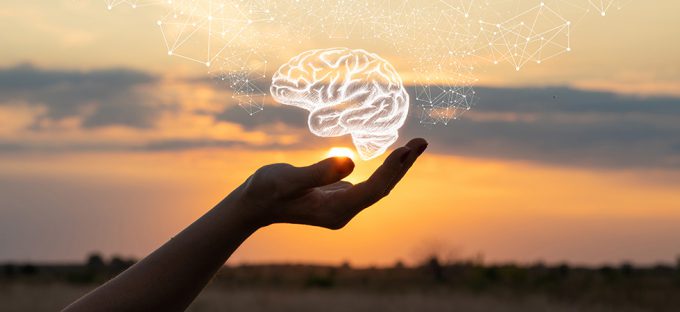 Hand holding a brain drawing against the sun and sky