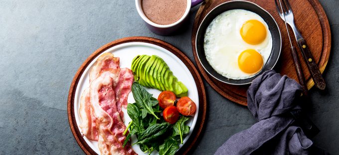 Bacon, avocado, eggs and tomato with keto coffee on a dark table and modern wooden plates with a grey linen napkin